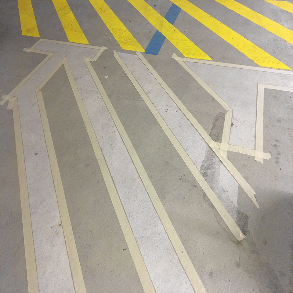 Beton padlóra festett fehér, sárga és kék csíkok és sávok, a parkoló készülő jelzései.